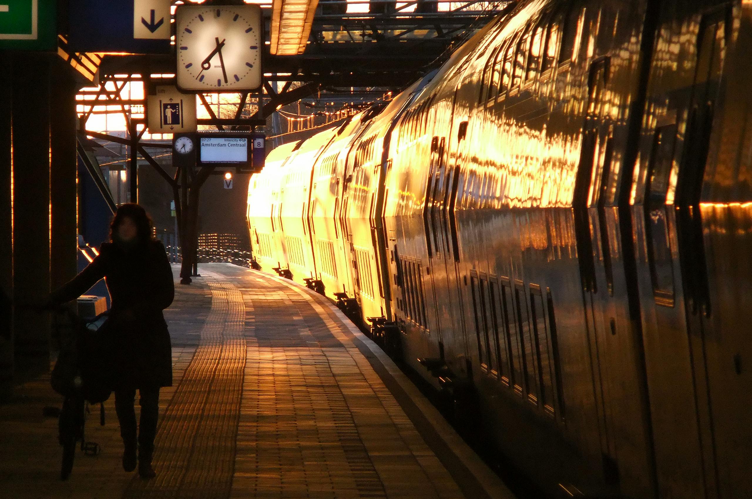 Silhouette of a person with a bike at Amsterdam Centraal Station during sunset. Train in golden light.